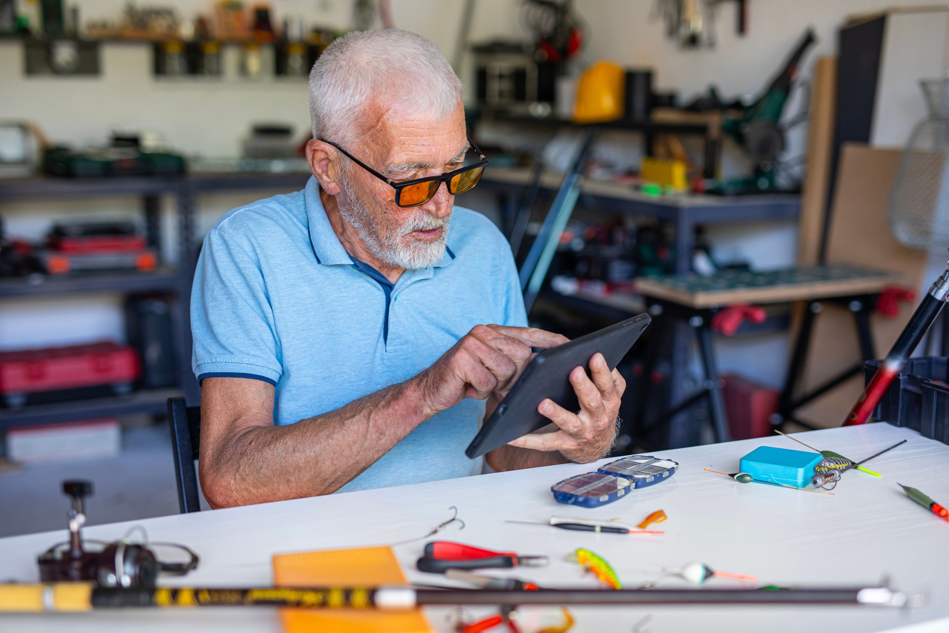 Retired senior watching tutorial on tablet while getting fishing equipment ready