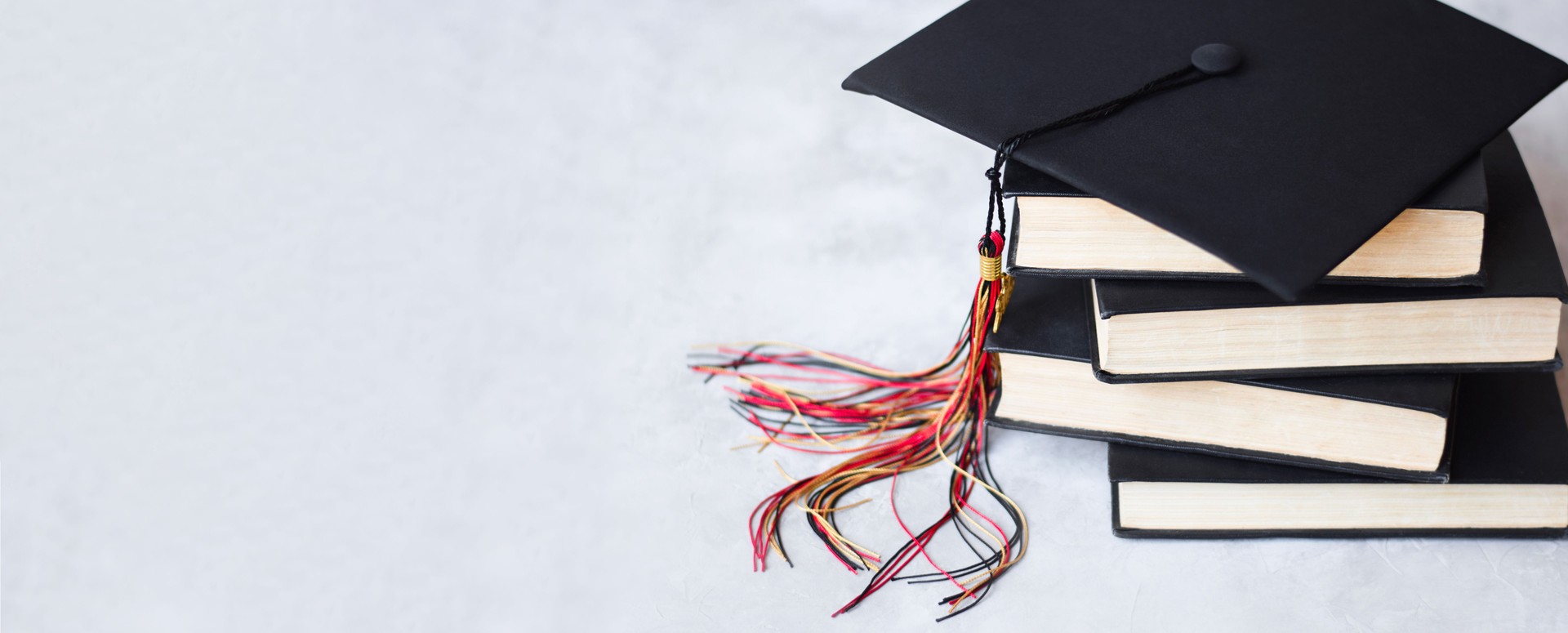 Graduation cap on top of stack of books on grey background